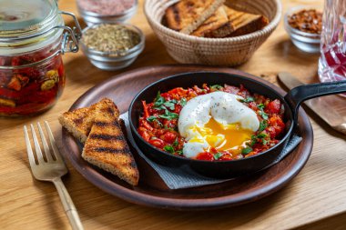 Kahvaltıda kızarmış tavada nefis shakshuka, yakın çekim. Haşlanmış yumurta, soğan, dolma biber, kırmızı domates ve yeşil maydanozdan ev yapımı shakshuka.