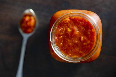Konserve taze sebzeli cam kavanoz, siyah arka planda leço. Ev yapımı konserve yiyecekler. Doğal ev yapımı kırmızı domates ve kaşık ile biber sosu. Üst görünüm, kapat
