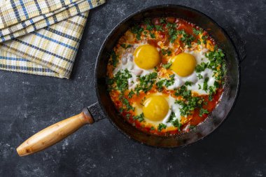 Shakshuka kahvaltıda kızartma tavasında, kapat. Kızarmış yumurta, soğan, dolma biber, kırmızı domates ve maydanoz karışımından yapılmış ev yapımı shakshuka dökme demir tavada, üst görünümde.