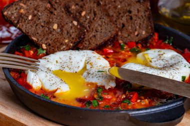 Kahvaltıda kızarmış tavada nefis shakshuka, yakın çekim. Haşlanmış yumurta, soğan, dolma biber, kırmızı domates ve yeşil maydanozdan ev yapımı shakshuka.