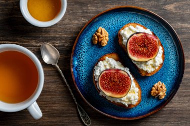 İki tane taze incir dilimli sandviç, beyaz süzme peynir, bal ve cevizli tost ekmeği tabakta, üst manzara, kapat. Sağlıklı beslenme. Lezzetli kahvaltı, öğle yemeği veya atıştırmalık