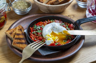 Kahvaltıda kızarmış tavada nefis shakshuka, yakın çekim. Haşlanmış yumurta, soğan, dolma biber, kırmızı domates ve yeşil maydanozdan ev yapımı shakshuka.