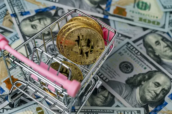 100 dolarlık banknotların arka planında küçük bir alışveriş arabasında bulunan kripto altın bitcoin paralar, yakın plan. Dijital para ve bitcoin kavramı