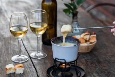 Lezzetli eritilmiş peynirli fondü, çatallar, ekmekler ve şarap ahşap masada, kapat.