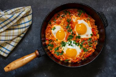 Shakshuka kahvaltıda kızartma tavasında, kapat. Kızarmış yumurta, soğan, dolma biber, kırmızı domates ve maydanoz karışımından yapılmış ev yapımı shakshuka dökme demir tavada, üst görünümde.