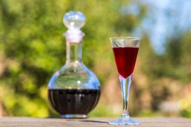 Şarap kadehinde ev yapımı kırmızı vişneli brendi ve yaz bahçesindeki ahşap bir masada cam bir şişede.