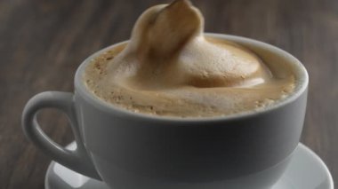 Tahta masada beyaz bardakta kaşıkla karıştırılmış sıcak kahve kapuçinosu köpüğü, yakın çekim. Süt köpüğü kapuçino, latte.