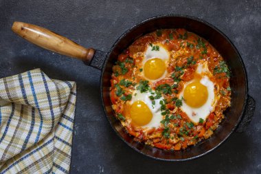 Shakshuka kahvaltıda kızartma tavasında, kapat. Kızarmış yumurta, soğan, dolma biber, kırmızı domates ve maydanoz karışımından yapılmış ev yapımı shakshuka dökme demir tavada, üst görünümde.
