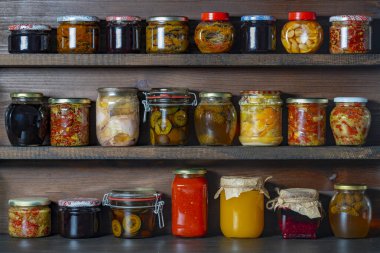 Kışın tüketim için mahzendeki ahşap raflarda cam kavanozlarda pek çok konserve yiyecek var. Kapatın. Gıda korunumu. Renkli turşu ve mayalanmış sebze kavanozları, bal, reçel ve diğer ürünler.