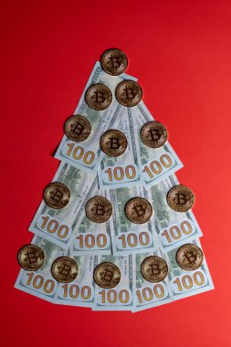 Kırmızı arka planda 100 dolarlık banknotlar ve bitcoin kripto paralarından yapılmış Noel ağacı, yakın plan. Yeni yılda finans, tasarruf, zenginlik, harcamalar temalı Noel dekoru