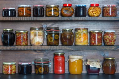 Kışın tüketim için mahzendeki ahşap raflarda cam kavanozlarda pek çok konserve yiyecek var. Kapatın. Gıda korunumu. Renkli turşu ve mayalanmış sebze kavanozları, bal, reçel ve diğer ürünler.