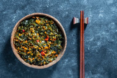 Healthy and fresh seaweed salad with carrot and pepper in wooden plate on dark background, close up. Seaweed its high iodine and calcium content makes it very good for nutrition for people clipart