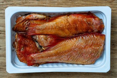 Beyaz plastik ambalajlı sıcak tütsülenmiş levrek balığı ahşap arka planda. Kapat, üst görünüm