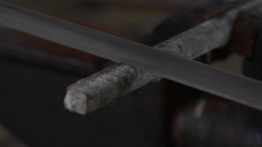 Bir adam demir bir çubuğu testere ile mengeneye sıkıştırıp testereyle kesiyor.