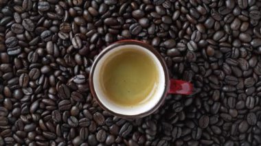 Red cup of hot black coffee with a rotating background of fresh roasted coffee beans, close-up, top view