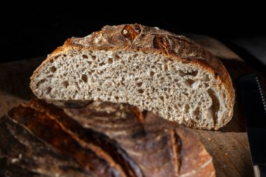 Tahta kesme tahtasının üzerinde yarım yuvarlak taze ekşi ekmek, yakın çekim. Rustik ekşi ekmek. Evde sağlıklı ekşi ekmek pişirmek.