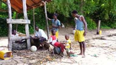 Zanzibar, Tanzanya - 16 Kasım 2019: Afrikalı erkek ve çocuklar Zanzibar, Tanzanya, Doğu Afrika kıyılarındaki gölgelerde bir gölgelik altında oturuyorlar.
