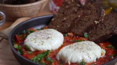 Kahvaltıda kızarmış tavada nefis shakshuka, yakın çekim. Haşlanmış yumurta, soğan, dolma biber, kırmızı domates ve yeşil maydanozdan ev yapımı shakshuka.