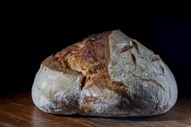 Tahta kesme tahtasının üzerinde taze pişmiş ekşi ekmeğin yuvarlak somunu, yakın çekim. Rustik ekşi ekmek. Evde sağlıklı ekşi ekmek pişirmek.