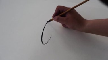 Bir sanat stüdyosundaki beyaz kağıda fırçayla resim çizen sanatçı erkek elin yakın çekimi.