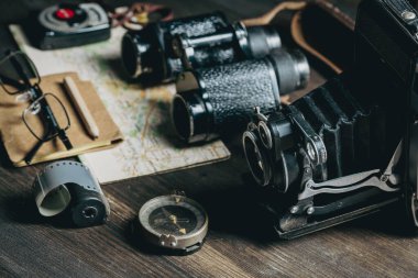 Eski model fotoğraf makinesi, dürbün, pusula, kağıt harita ve tahta bir masanın üzerindeki gözlükler. Yolculuk ya da keşif için hazırlanmış ve planlanmış eşyalar
