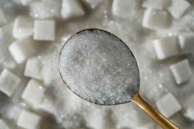 Beyaz granüllü şeker arka plandaki şeker küplerinde, üst manzara, kapat. Sağlıksız yeme, obezite, kalp hastalığı, diyabet kavramı.