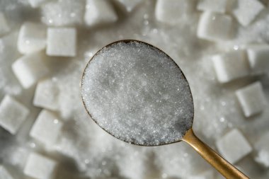 White granulated sugar in spoon in the background pile sugar cubes, top view, close up. The concept of unhealthy eating, obesity, heart disease, diabetes clipart