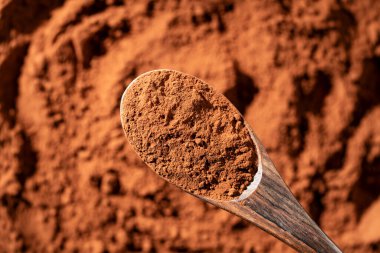 Arka planda tahta kaşıkta doğal koyu kahverengi kakao tozu, üst manzara, yakın çekim. Bir yığın organik kakao tozu.