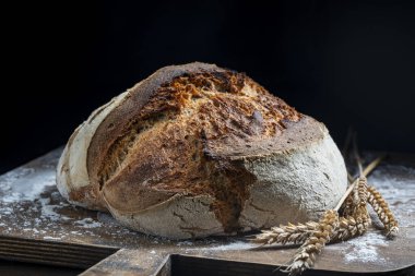 Tahta kesme tahtasının üzerinde buğday kulaklı taze ekşi ekmeğin yuvarlak somunu, yakın çekim. Rustik ekşi ekmek. Evde sağlıklı ekşi ekmek pişirmek.