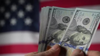 Amerikan bayrağının arka planına karşı 100 dolarlık banknotlar yığını, yakın plan. Finans, iş, ekonomi ve paranın güvenilirliği kavramı