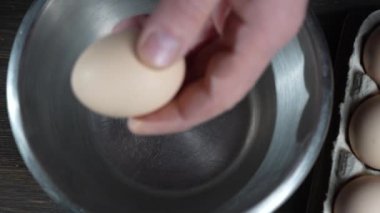 Bıçaklı adam mutfakta çiğ tavuk yumurtasını kaseye kırar, yakın plan, üst manzara. Omlet pişirme, kahvaltı, öğle yemeği, sağlıklı yemek ve yemek pişirme kavramı. 