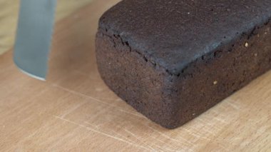 Tahta kesme tahtasının üzerinde siyah ekmek dilimleri. Bir bıçakla bütün tahıllı ekmeği kes. Koyu ekmeğe yakın, sağlıklı bir yaşam tarzı.