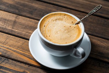 Sıcak kahve kapuçinosu köpüğü. Tahta masada beyaz bardakta kaşık, yakın çekim. Süt köpüğü kapuçino, latte.