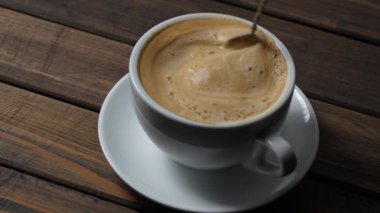 Tahta masada beyaz bardakta kaşıkla karıştırılmış sıcak kahve kapuçinosu köpüğü, yakın çekim. Süt köpüğü kapuçino, latte.