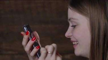 Mutlu ve rahat genç kız elinde akıllı bir telefonla cep telefonu ekranına bakıyor. Evde sosyal medyada gülüyor ve sohbet ediyor. Kapat. Neşeli kız cep telefonuna mesaj yazıyor, kapalı bir yerde. 