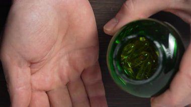 Kıdemli adam balık yağı kapsülünü elden ele dolduruyor, kapalı alanda, yakın mesafeden. Omega 3 ve D vitamini içeren altın balık yağı kapsülü. Doğal tıp, sağlıklı yaşam tarzı ve beslenme konsepti.