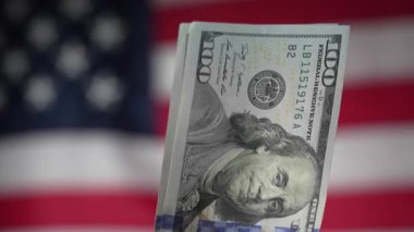 Amerikan bayrağının arka planına karşı 100 dolarlık banknotlar yığını, yakın plan. Finans, iş, ekonomi ve paranın güvenilirliği kavramı