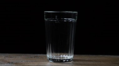 Siyah arka planda, ahşap bir masanın üzerindeki cam parçalarına su dökerek.