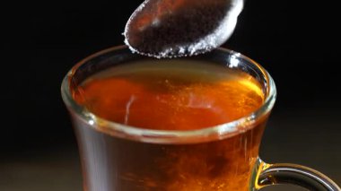 Sıcak Türk çayıyla kaşıktan bardağa beyaz şeker dökmek.