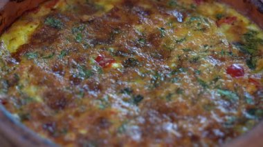 Ceramic bowl with vegetable frittata, simple vegetarian food. Frittata with tomato, pepper, onion and cheese on wooden table, close up. Italian egg omelette, rotates