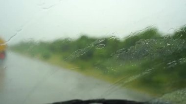 Ön cama yağmur damlaları düşer ve araba silecekleri suyu temizler. Arabanın ön camında yağmur damlalarıyla içeriden yağmur manzarası seyrediyor. Arabanın ön camına yağmur yağıyor. Tanzanya, Afrika. Yavaş çekim