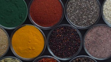 Arka planda farklı baharatlar ve bitkiler dönüyor, yakın plan, üst görünüm. Renkli baharatlar, tohumlar ve yemek pişirmek için bitkiler.