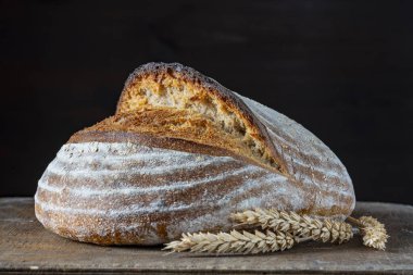 Tahta kesme tahtasının üzerinde buğday kulaklı taze ekşi ekmeğin yuvarlak somunu, yakın çekim. Rustik ekşi ekmek. Evde sağlıklı ekşi ekmek pişirmek.