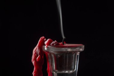 Sönmüş kırmızı bir mumun dumanı siyah bir arkaplanda cam bir şamdanın içinde, yakın.