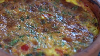 Ceramic bowl with vegetable frittata, simple vegetarian food. Frittata with tomato, pepper, onion and cheese on wooden table, close up. Italian egg omelette, rotates