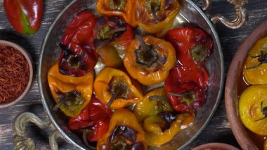 Baked red and yellow tomato and bell pepper. Tomatoes and bell peppers in a baking dish on a wooden table. A healthy and delicious vegetarian dish. Close up, top view, rotates