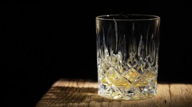 Siyah arka planda şişeden kristal bardağa viski dökmek, yakın plan. Barmen bardağa alkolü doldurur, ağır çekimde.