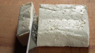 Şefin elleri tahta kesme tahtasıyla taze beyaz süzme peynir dilimlerini kesiyor. İnek sütünden ev yapımı beyaz peynir