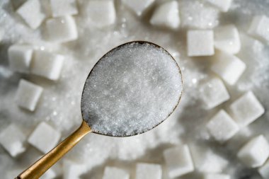 Beyaz granüllü şeker arka plandaki şeker küplerinde, üst manzara, kapat. Sağlıksız yeme, obezite, kalp hastalığı, diyabet kavramı.