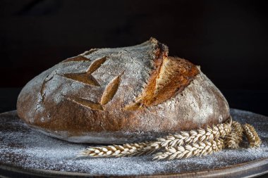 Tahta kesme tahtasının üzerinde buğday kulaklı taze ekşi ekmeğin yuvarlak somunu, yakın çekim. Rustik ekşi ekmek. Evde sağlıklı ekşi ekmek pişirmek.